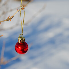 red ball - a Christmas toy lies in the snow on a sunny day.