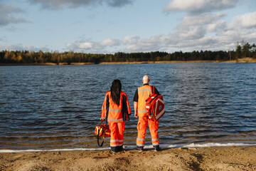 Two proud paramedics posing near blue lake on sunny day