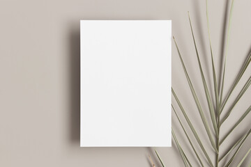 White invitation card mockup with a palm leaf on a beige table. 5x7 ratio, similar to A6, A5.