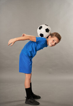 Cute Boy With Soccer Ball On His Back Standing Against Gray Background