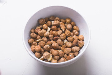 Photo from above of a bowl with hazelnuts on white background.