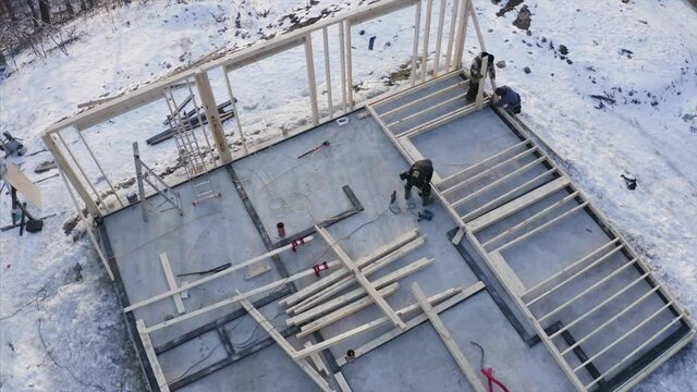 Aerial panoramic view of the frame house under construction. Laborers are adjusting wooden balks of a future wall. Winter day