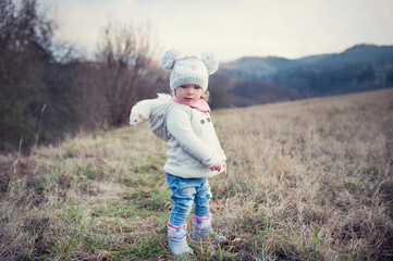 A little girl is outside with her pet. Cute baby girl wearing a ferret in a hood. The child and his...