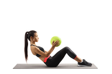 Fototapeta na wymiar Full length profile shot of a young woman sitting on a mat and exercising with a ball