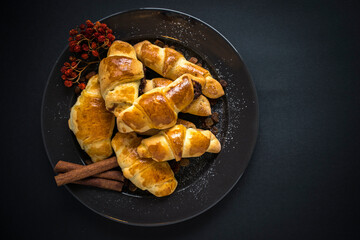 Freshly baked sweet homemade rolls with jam sprinkled with powdered sugar and cinnamon, served on a plate on a dark background.