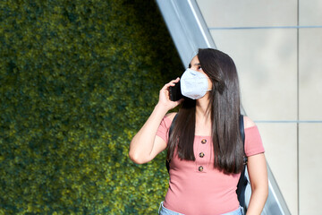 young woman wearing mask talking on smart phone looking up
