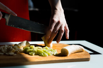 Woman's hands cutting fresh banana on the wooden board on the kitchen