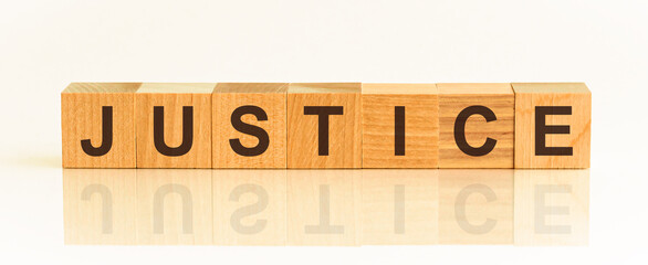 Wooden blocks with the text: justice. The text is written in black letters and is reflected in the mirror surface of the table.