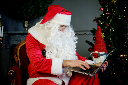 Man In Santa Claus Suit Is Sitting In Living Room And Chatting By Laptop With Video Chat. Close Up