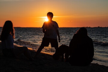 Fototapeta premium silhouette of a boy and some family members in the beautiful sunset. Enjoying the peaceful scenery while playing with his dog