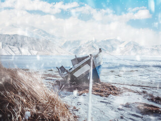 frozen lake and old fishing boat on the background of mountains in the snow.