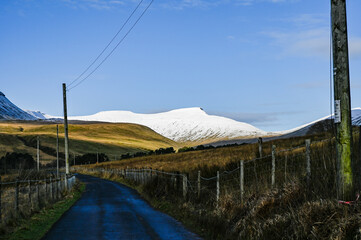 View of pen y fan peak from a distance with snow on top during the winter months in south wales uk. many walkers ontop taking in the views.