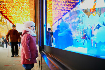 Toddler girl looking at window glass of large department store decorated for Christmas