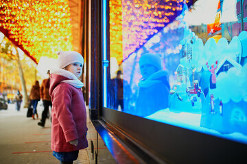 Toddler girl looking at window glass of large department store decorated for Christmas