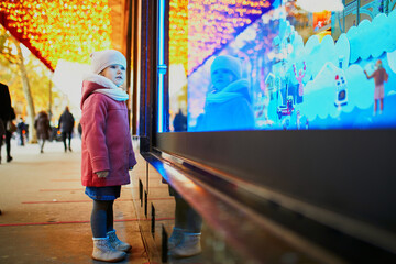 Toddler girl looking at window glass of large department store decorated for Christmas