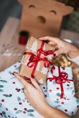 A woman holding a Christmas gift over other presents located below. Christmas presents concept. Close up. Selective focus.