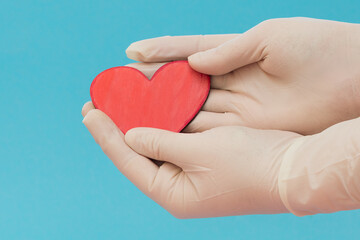 Obraz premium Hands in medical gloves hold a small red heart on a blue background. Protection from covid-19. Stay safe. Gratitude to doctors. Valentine's day.Horizontal photo, side View, close-up.