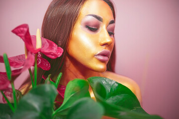 Fototapeta premium Girl with dark hair and golden mask on her face on a pink background