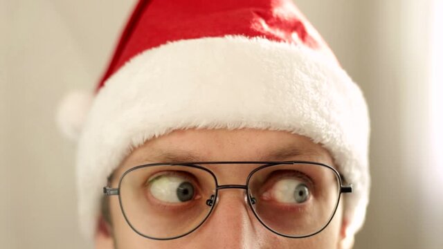 Young funny elf man in spectacles and christmas hat peek out and look around surprisingly