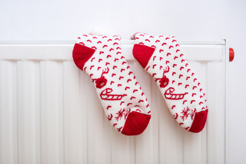 White and red christmas socks hanging on warm central heat radiator, winter holiday home mood