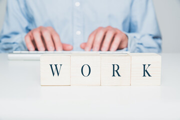 Wooden cubes with the word WORK, in the background a man working on the keyboard. Office work concept.