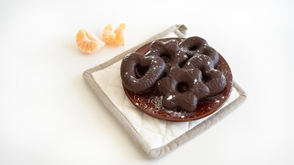 Homemade gingerbread covered with chocolate on brown ceramic plate, clementine slices, white background 