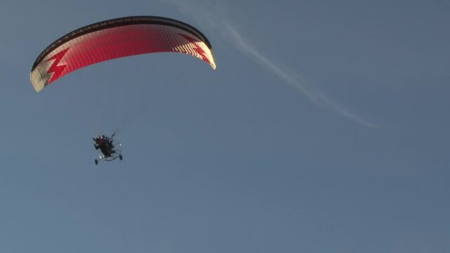 Flight of a motorized paraglider against a blue sky. Opening of the Celestial Fair festival.