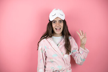 Pretty girl wearing pajamas and sleep mask over pink background showing and pointing up with fingers number four while smiling confident and happy