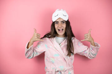Pretty girl wearing pajamas and sleep mask over pink background shouting with crazy expression doing rock symbol with hands up