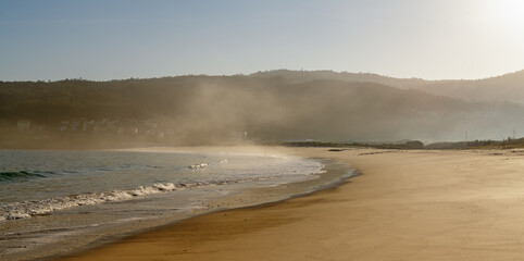 fog and mist rising from a golden sand beach with gentle lapping waves