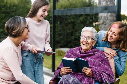 Latina Grandmother Reading A Book To Her Granddaughter In A Backyard Outside Home In Mexico City