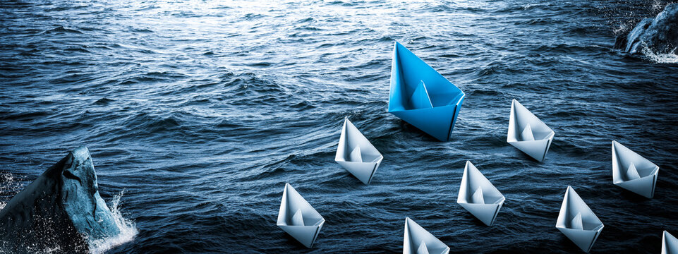 Blue Paper Boat Leading A Fleet Of Small White Boats Around Rocks In Rough Water - Leadership Concept