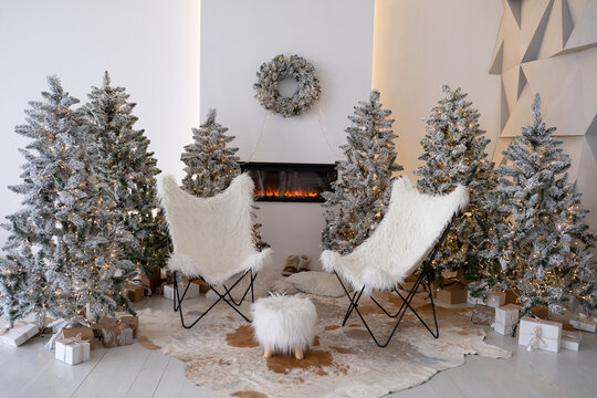 New Years bright chalet interior with decorated Christmas trees with garlands and comfortable white armchairs near the fireplace. Christmas interior. Scandinavian style. Location for photo shoot.