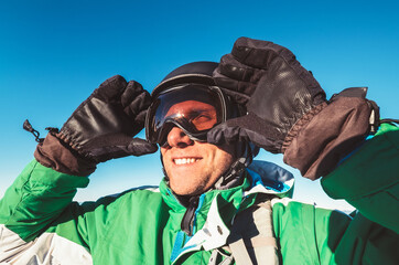 Smiling skier or snowboarder man portrait in safe ski helmet and goggles with blue sky background....