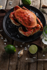 View from above of black round plate with cooked crab served with ice cubes, seashells and lime on wooden background. Delicious meal. Seafood concept. Space for text. Space for text. Restaurant menu.