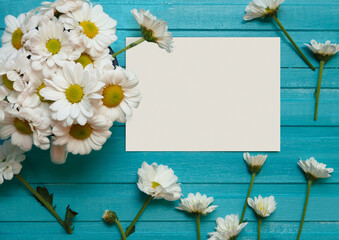 Greeting card mockup with daisies. Bright blue wooden background with chamomile. Minimalism concept. Floral backdrop. Top view. Perfect for presentations, decor and web design.