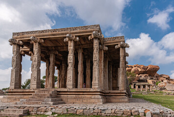 Hampi, Karnataka, India - November 4, 2013: Ruinous Kadelekalu Ganesha temple in front of other ruins and brown boulders under blue cloudscape.