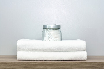 A view of a glass jar of personal hygiene items that stands on two neatly folded towels.