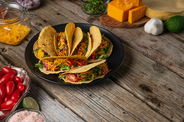 Plate with tasty mexican tacos on rustic wooden table with ingredients for cooking background. Concept of traditional meal. Side view.