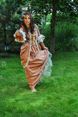 Obraz na płótnie Canvas A girl dressed as a princess or fairytale fairy playing with bubbles on the grass