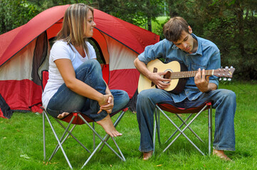 Man and woman playing the guitar in camping chairs while camping