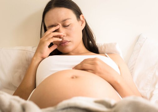 A stressed tired pregnant mother lying in bed at home. Morning sickness and nausea.