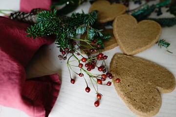 Arrangement of holiday objects and decorations -- green spruce, red berries, ginger heart cookies.
