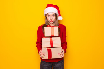 Young woman with Christmas hat holding a gift isolated on yellow background.