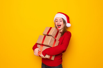 Pretty overjoyed woman holding giftbox close to chest wear knitted jumper and santa hat isolated yellow background
