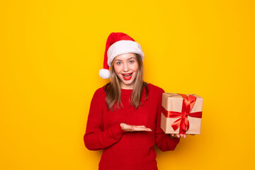 Woman with Christmas hat holding a gift on yellow background.
