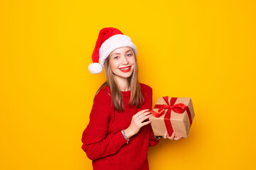 Woman with Christmas hat holding a gift on yellow background.