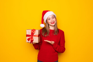 Young woman with Christmas hat holding a gift isolated on yellow background.