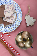 Vintage porcelain, various Christmas decorations and chocolate pieces. Flat lay, pink background.