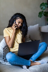 Portrait of a woman speaking on cellphone in front of her laptop at home